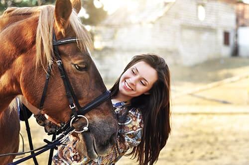 Smiling woman petting a horse during equine assisted therapy session.