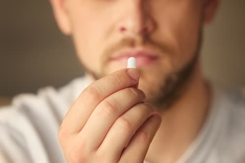 Out of focus man holding up a pill that may indicate OxyContin drug abuse.