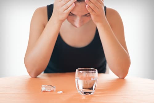Woman at table with pills on it, hands on head dealing with speed drug abuse.