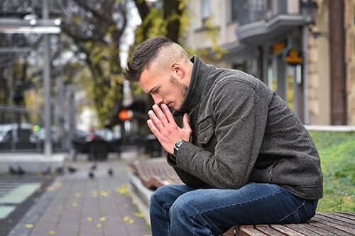 Young man with folded hands on bench worried about his Kratom abuse