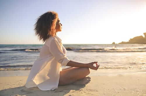 Woman meditating on beach participating in holistic drug therapy