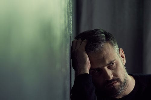 Sad man in dark against wall may need an addiction and depression treatment program