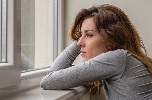 Depressed woman looking out window wondering what is alprazolam