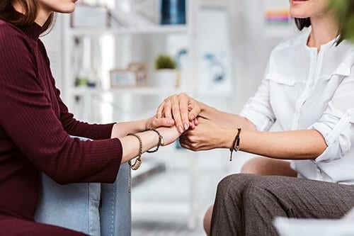 Two women holding hands during a session of addiction therapy services in florida at Beaches