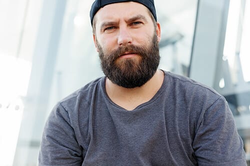 Bearded man in hat confused about where to find cross addiction treatment