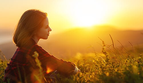 Woman sitting in sunset field trying to find faith based addiction recovery programs