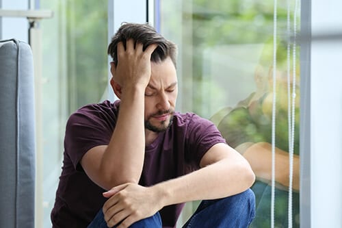 Visibly depressed man at window probably needs mood disorders treatment during addiction rehab