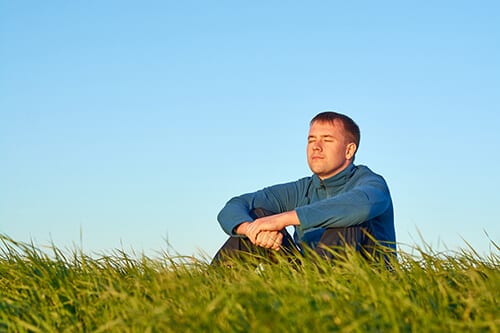 Man relaxing in a field breathing through quotes about mindfulness