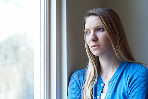 Woman looking out window worried about opioid addiction recovery