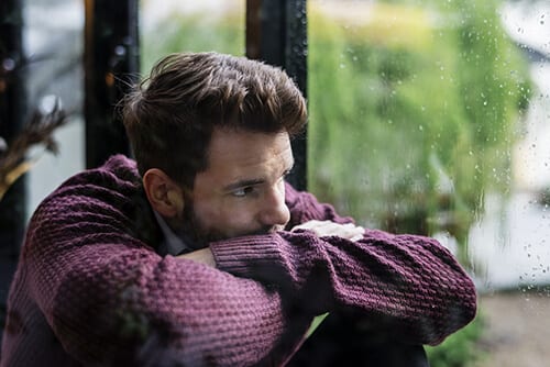 Man resting on arms looking out window contemplating the stages of drug addiction
