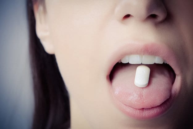 a woman holds a pill on her tongue thinking about the long term effects of xanax