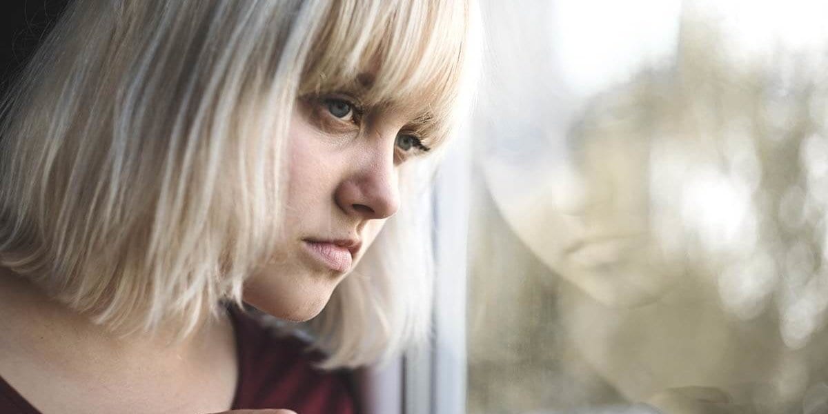 Young woman looking out window showing physical signs of heroin abuse