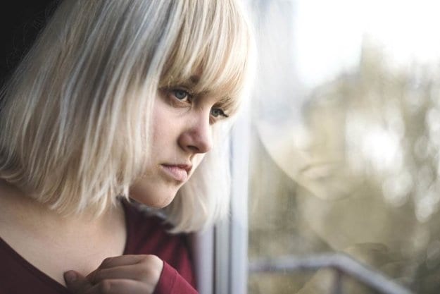 Young woman looking out window showing physical signs of heroin abuse