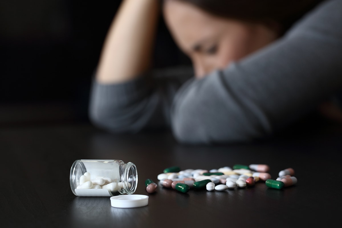 Pills spilled on the table next to a woman struggling with clonazepam abuse