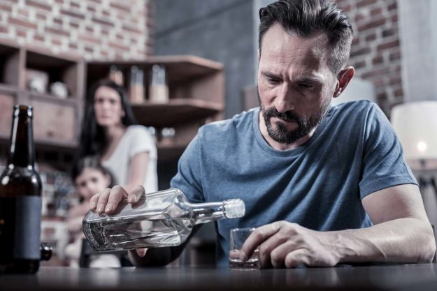 family shying away from man pouring another shot of whiskey showing the need for alcohol addiction treatment in florida