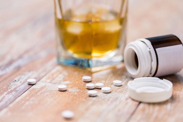 pills spilling out of bottle next to glass of alcohol posing the question of how to talk to your kids about kids drug and alcohol abuse