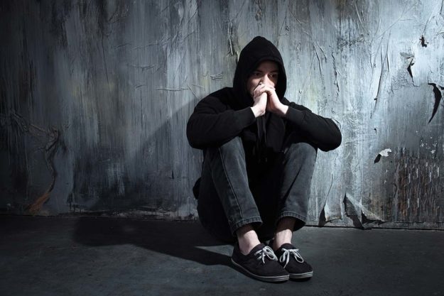 man curled up sitting on floor wondering about the common risk factors for addiction