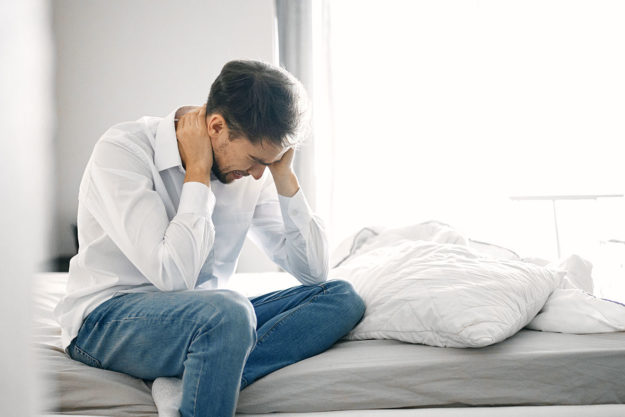 man on bed with head in hands concerned about compromised immune system