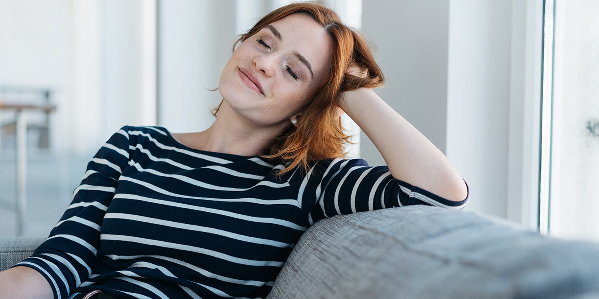 woman lounging on couch smiling due to Stress Management to stay sober