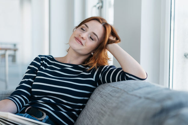woman lounging on couch smiling due to Stress Management to stay sober